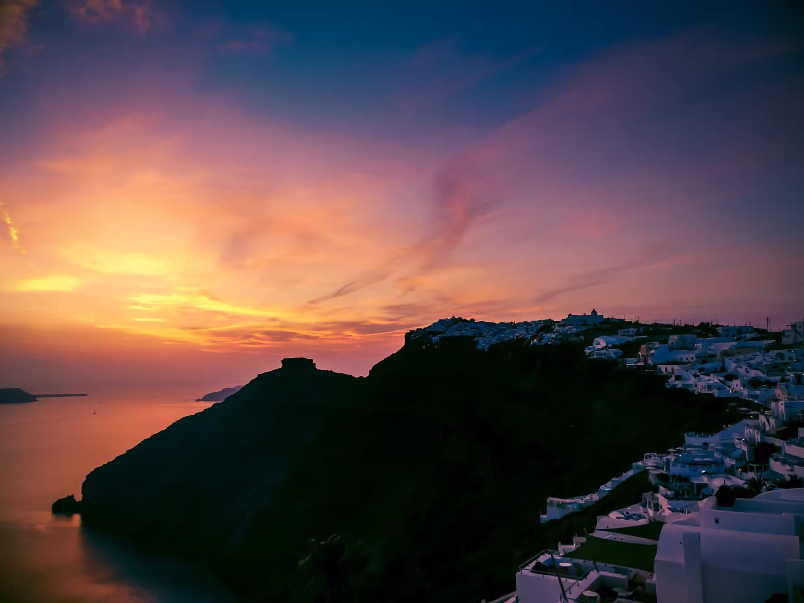 Coucher de soleil depuis la corniche de Fira, facades blanches dorées et caldeira illuminée